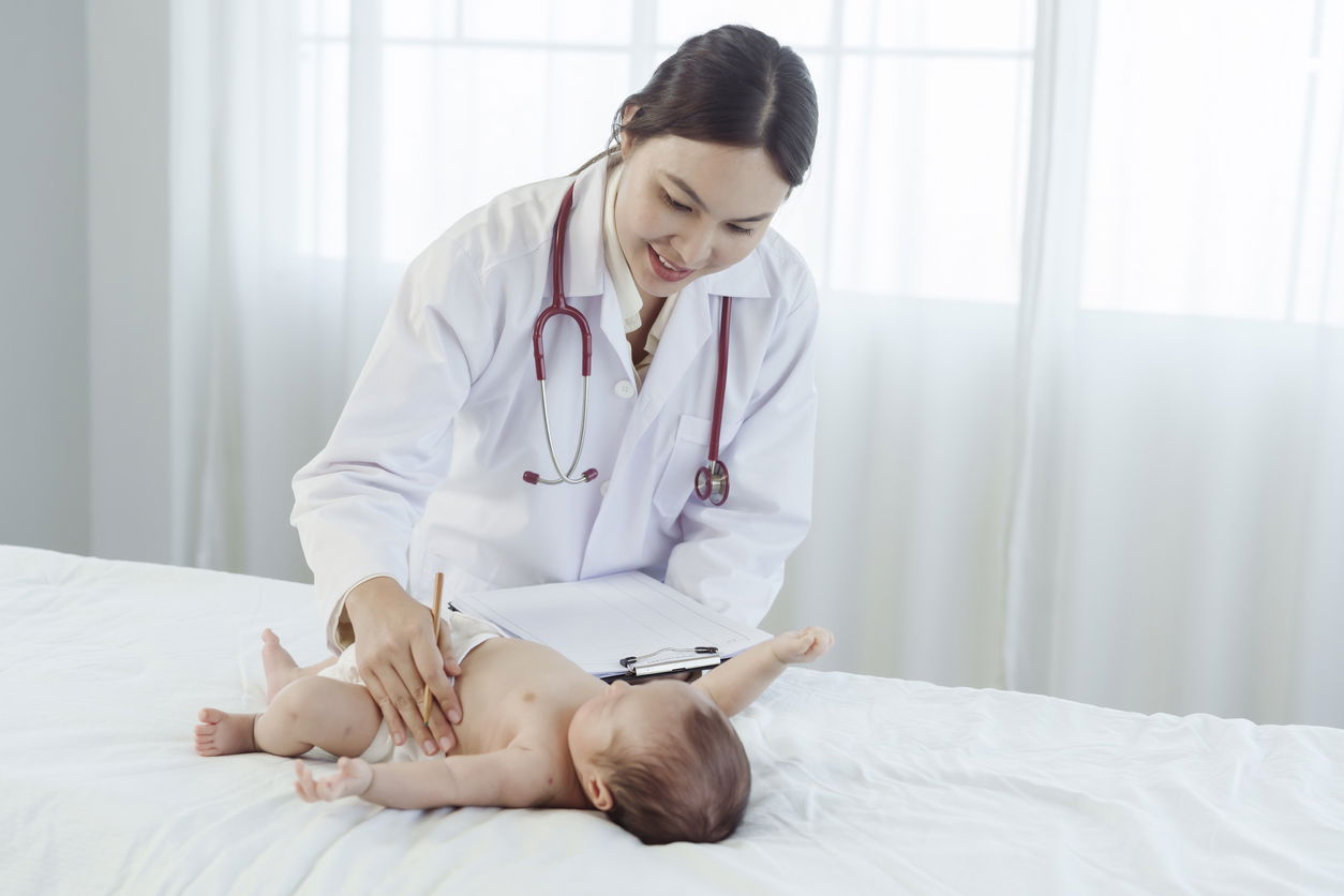 Asian woman who is a pediatrician Health check of sick newborn baby lying on white bed in hospital examination room